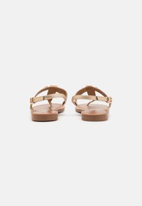 Sandales à brides avec une semelle plate, couleur tan, avec une finition lisse et un accent en métal doré sur les brides.
