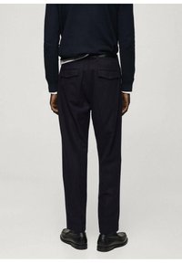 Pantaloni închisi navy, realizați dintr-un material texturat, având două buzunare la spate cu clapete și o croială slim. Purtați cu un top negru și pantofi negri.