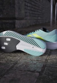 Jasnoniebieskie buty do biegania z teksturowanym wierzchem i czarnymi akcentami. Posiadają wielokolorową podeszwę z charakterystycznym detalem marki ADIZERO.