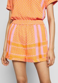Pantaloni corti arancioni e rosa con una vita elastica, caratterizzati da vari motivi geometrici e un fit comodo e casual.