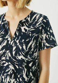 Top a maniche corte in blu navy con motivo astratto bianco, caratterizzato da scollatura a V e sottile dettaglio della tasca, realizzato in tessuto testurizzato.