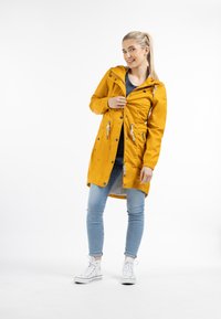 Jachetă de ploaie galbenă cu fermoar, talie cu șnur și multiple buzunare. Purtați-o peste un top cu dungi, asortat cu blugi ușor albaștri și adidași albi.