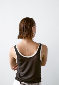 Hnědý tílko s bílým lemem, měkká tkanina, přiléhavý tvar a široké ramínka. Pohled zezadu ukazuje detaily ramen a krku.