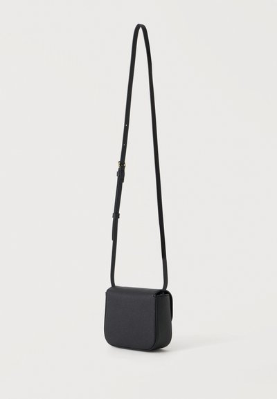 Μαύρη δερμάτινη τσάντα crossbody με ρυθμιζόμενο λουράκι, κρεμασμένη σε απλό φωτεινό φόντο.