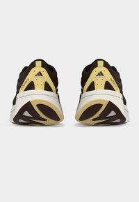 Mustade ja beežide Adidas Adizero jooksujalatsite paar nähtud tagant, rõhutades paksu valget tallad ja logode detaile.