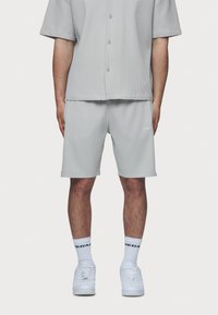 Grijs overhemd met korte mouwen en knoopsluiting, met een geribbelde textuur, en bijpassende grijze shorts. Witte sneakers met gestructureerde zolen en halflange witte sokken.