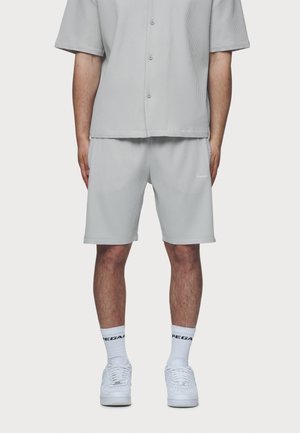 Chemise grise à manches courtes et boutons avec une texture en relief et un short gris assorti. Baskets blanches avec des semelles texturées et chaussettes blanches arrivant au mollet.