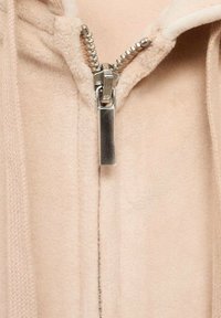Gros plan sur une veste polaire beige partiellement zippée montrant un curseur et des dents de fermeture éclair en métal argenté.
