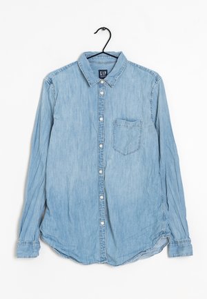 Light blue long-sleeve denim shirt with front buttons and chest pocket hanging on a black hanger against a white background.