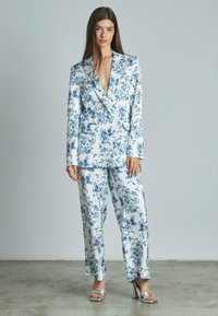 Polls classique en blanc et bleu, avec un décolleté en V profond et des revers surdimensionnés, fabriqué à partir d'un tissu lisse avec une coupe décontractée. Sandales à talons argentées.