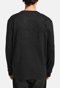 Zwarte langmouw T-shirt met reliëftekst en wereldbolontwerp op de achterkant. Gemaakt van katoen, met een ronde hals en rechte zoom.