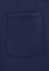 Tessuto blu navy con una tasca a toppa rettangolare caratterizzata da bordi doppia cucitura e angoli inferiori arrotondati.