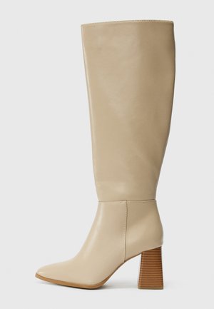 Beige Lederstiefel bis zum Knie mit spitzem Zehenbereich, strukturiertem Blockabsatz und glatter Oberfläche. Nahtdetails an Knöchel und oberem Schaft.