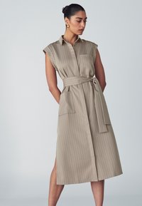 Beige ärmelloses Hemdkleid mit vertikalen Streifen, Taillengürtel und einer Seitentasche, mit Kragen und mittellangem Schnitt. Glatte Stoffstruktur.