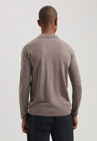 Pulover cu mânecă lungă, de culoare maro, cu guler, fabricat dintr-un material moale. Textură netedă, cu o formă ajustată, având hem drept și fante laterale.
