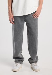Vaqueros de denim gris con un corte holgado, puños elásticos, textura sutil y una cintura de altura media. Combinados con zapatillas blancas.