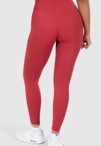 Red high-waisted leggings made of stretchy fabric, fitted design accentuating legs, paired with white athletic shoes and patterned socks.