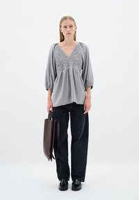 Hallhalli pluus smockitud bodice'iga, V-kaelusega ja puhvärviga. Kombineeritud kõrge vöökoha mustade teksade ja pruuni kotiga. Mustad jalanõud.