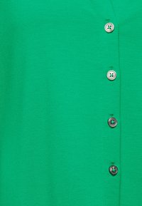 Tissu vert avec une rangée verticale de cinq boutons, trois blancs en haut et deux boutons gris plus foncés en dessous.