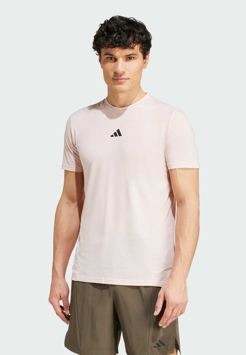 T-shirt rose clair à manches courtes en tissu doux, avec un logo triangulaire noir sur la poitrine et un col camionneur.