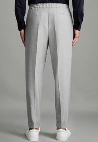 Pantaloni gri deschis cu un finisaj texturat, pliuri la spate, talie elastică și manșete răsucite, asortați cu adidași albi.