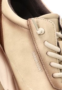 Zapato de cuero beige con textura suave, forma redondeada y detalles de costura sutiles. Los cordones son de color claro y los ganchos son mínimos.