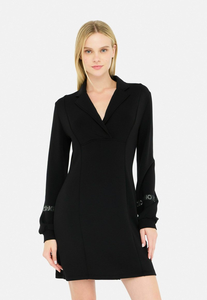 Abito lungo nero con maniche, colletto, design aderente, texture liscia e dettagli accentuati ai polsini.