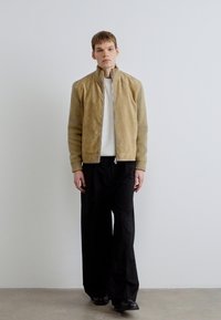 Tansuvine jakk soonikkoeliste varrukatega, luku sulgumise ja kõrge kraega. Sobitatud valge soonikkoelise särgi ja mustade laiade pükstega.