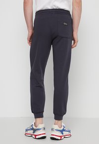 Marine joggerbroek gemaakt van zachte stof, met een achterzak en een elastische tailleband, gecombineerd met multi-kleurige sneakers.