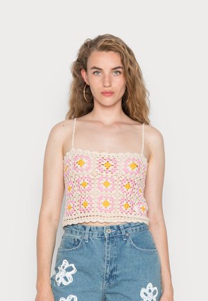 Top de crochê em bege com padrões florais em rosa e amarelo, destacando alças finas e um decote em formato escalope. Combinado com calções de ganga de cintura alta.