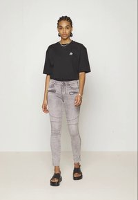 T-shirt oversized de algodão preto com logótipo branco, combinado com jeans skinny cinzas com bolsos com fecho e detalhes de costura. Sandálias pretas com plataforma.