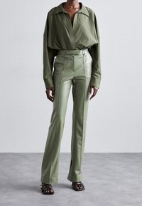 Chemise boutonnée oversize en vert olive, avec un large col, associée à un pantalon en cuir ajusté et brillant taille haute de couleur assortie.