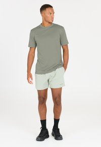 Vihreä oliivinvärinen urheilupaita, kevyt kangas, pyöreä kaula-aukko. Vaaleanharmaat shortsit, joustava vyötärö, polven ylle ulottuvat, yhdistetty mustiin lenkkikenkien ja sukkien kanssa.