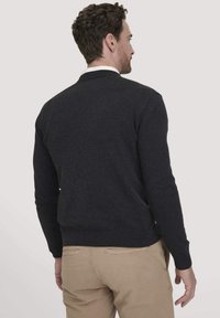 Dunkelgrauer Strickpullover mit Rundhalsausschnitt, gerippten Bündchen und Saum. Weiche Textur, taillierte Passform, getragen über hellen Hosen.