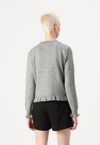 Grå strikkegenser med rund hals, ribbet mansjetter og en slitt søm. Stylet med svarte shorts. Myk tekstur og avslappet passform.