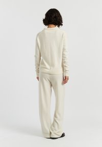 Helles beigefarbenes Strickpullover mit einem gerippten Rundhalsausschnitt, kombiniert mit passenden weiten Hosen. Weiche Textur, lockere Passform und minimale Nähdetails.