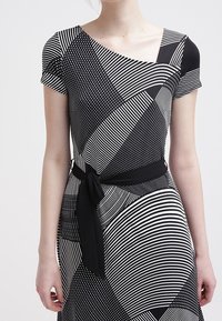 Svart och vit mönstrad klänning med korta ärmar, som har diagonala ränder och prickar, åtdragen vid midjan med ett tygbälte.