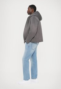 Grå huvtröja i mjukt tyg, kombinerad med ljusblå jeans och vita sneakers. Jackan har en framzipper och en avslappnad passform.