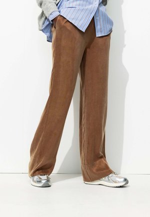 Pantalons larges marron en tissu doux, avec une texture subtile. Associés à des baskets argentées et une chemise rayée bleu clair.