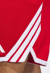 Pantalones cortos atléticos rojos con una tela texturizada y transpirable. Presenta rayas de acento blancas a lo largo del costado y un diseño de dobladillo en contraste.