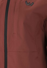 Vattenavvisande brun jacka med strukturerad yta, utrustad med svarta dragkedjor, en bröstficka och en logotypaccent.