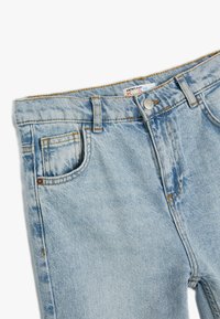 Vaqueros de mezclilla azul claro con un acabado descolorido, diseño de cinco bolsillos, cierre de botón metálico y costuras amarillas a lo largo de las costuras.