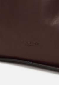 Bruine leren tas met een gladde textuur en reliëfbranding "Marc O'Polo" en "opgericht in Stockholm" op het oppervlak.