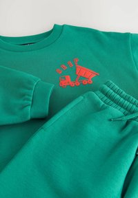 Grön sweatshirt och matchande joggers i mjukt tyg. Har en röd lastbilsgrafik med ordet "BEEP" på sweatshirten. Elastisk midja.