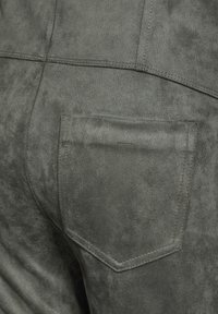 Grå mockastickade byxor med en bakficka med rundad design och synliga sömmar, som framhäver en mjuk textur.