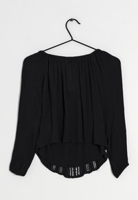 Blouse noire légère avec des manches longues, design décolleté, col froncé et dos transparent avec garniture décorative.