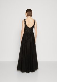 Rochie de seară neagră cu spatele descoperit, cu detalii din dantelă și un corset ajustat. Fusta este amplă și realizată dintr-un material fluid.
