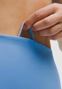 Modré plavky s hladkou textúrou, na ktorých sa nastavuje tenký popruh rukou. Dizajn je minimalistický a priliehajúci.