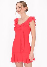 Robe courte rose en tissu léger, avec des manches volantes, un décolleté carré et un ourlet évasé agrémenté d'un lien.