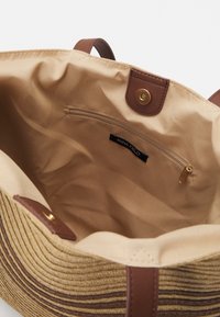 Brązowa i beżowa torba tote w paski z gładkim wnętrzem, z zapinaną na zamek kieszenią i skórzanymi detalami. Oznaczona napisem "ANNA FIELD."